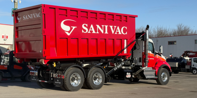 Camion Sanivac transportant un conteneur roll-off rouge en position levée devant la succursale