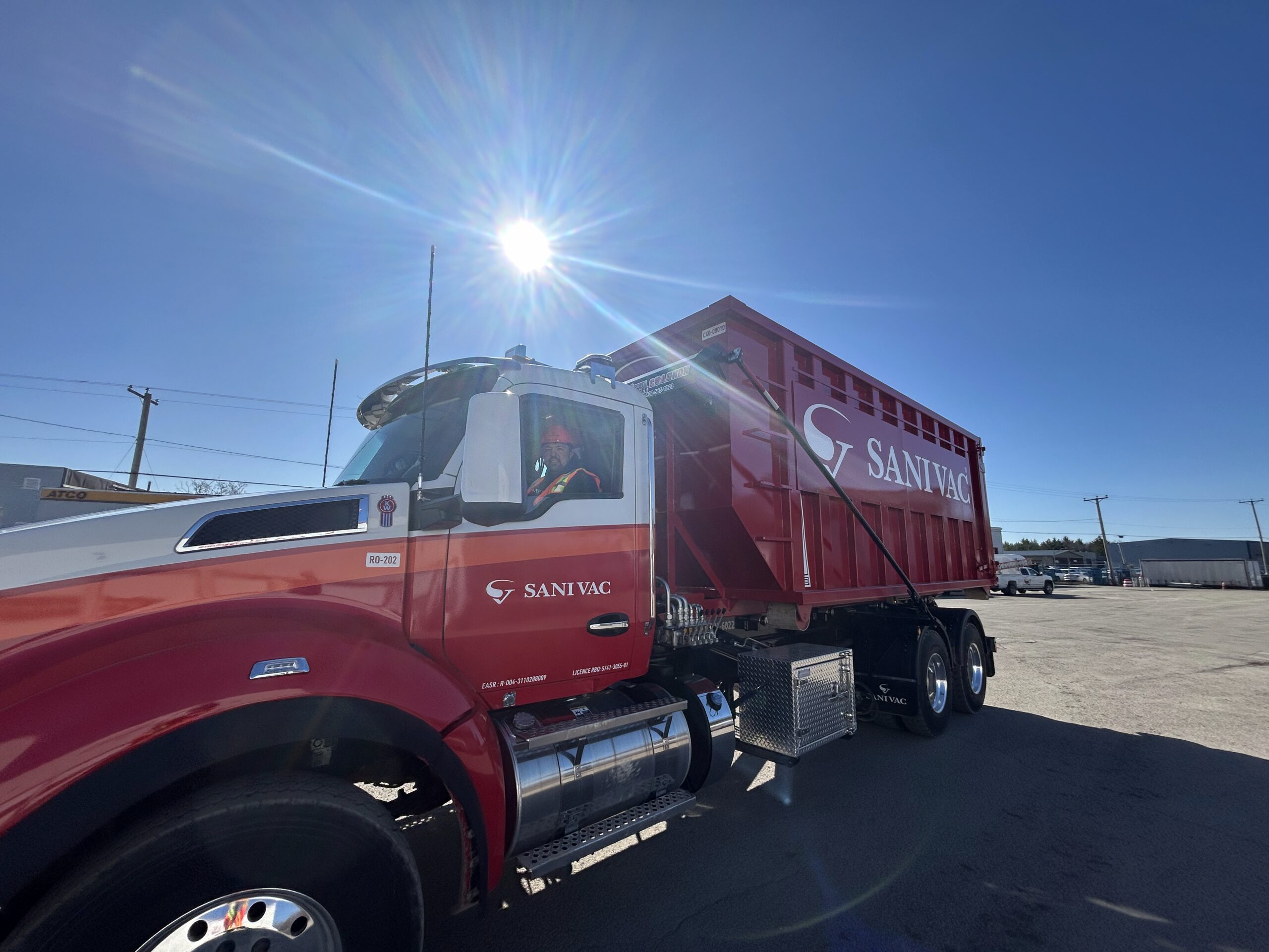 Camion Sanivac transportant un conteneur rouge en direction d’un chantier